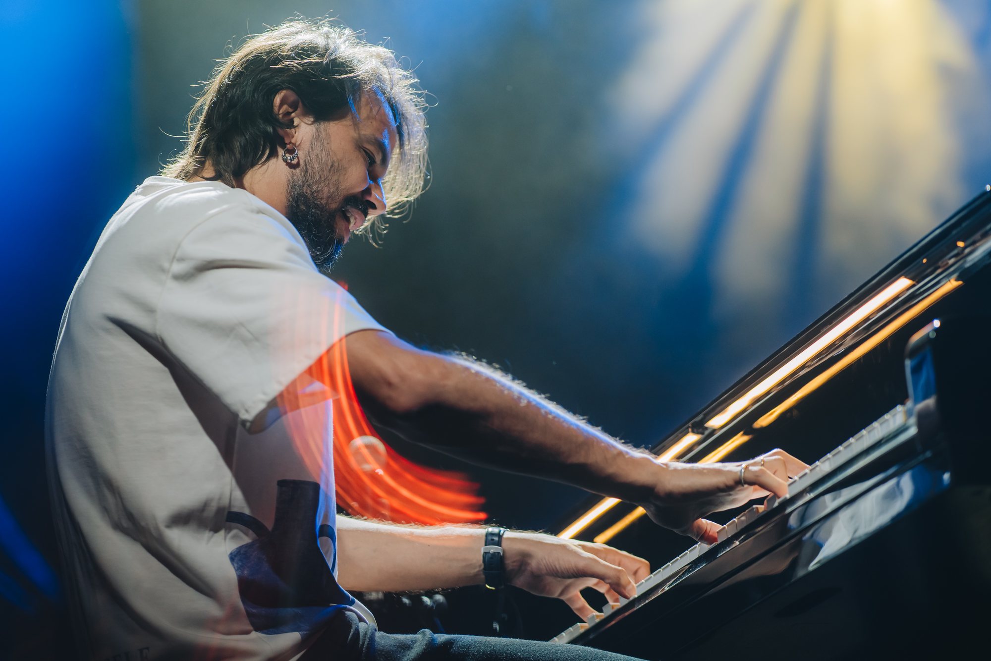 Salomão Soares ao piano de cauda, sorrindo, com um rastro de luz laranja acompanhando o braço